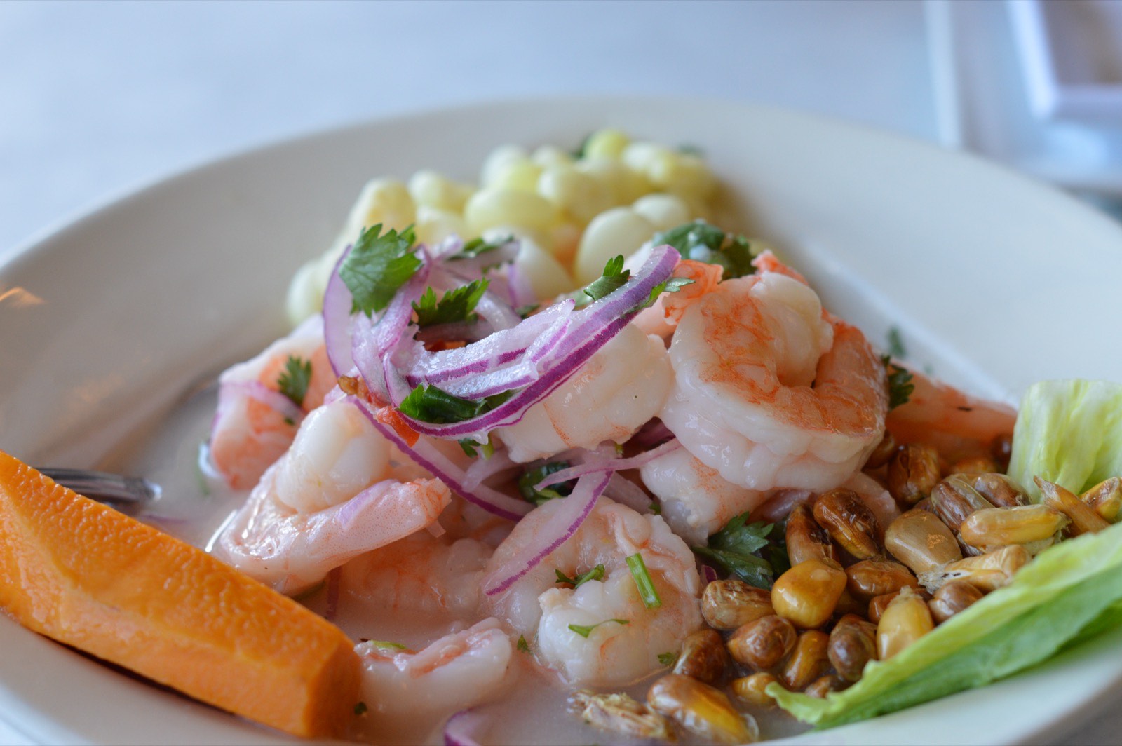 Ceviche de pescado y camarón con cebolla roja, camote y choclo